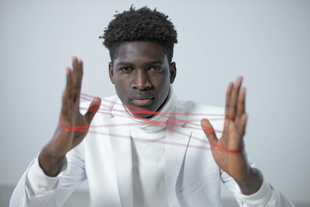 Close-up portrait of a man in a white suit manipulating red string between his hands with focus and precision.
