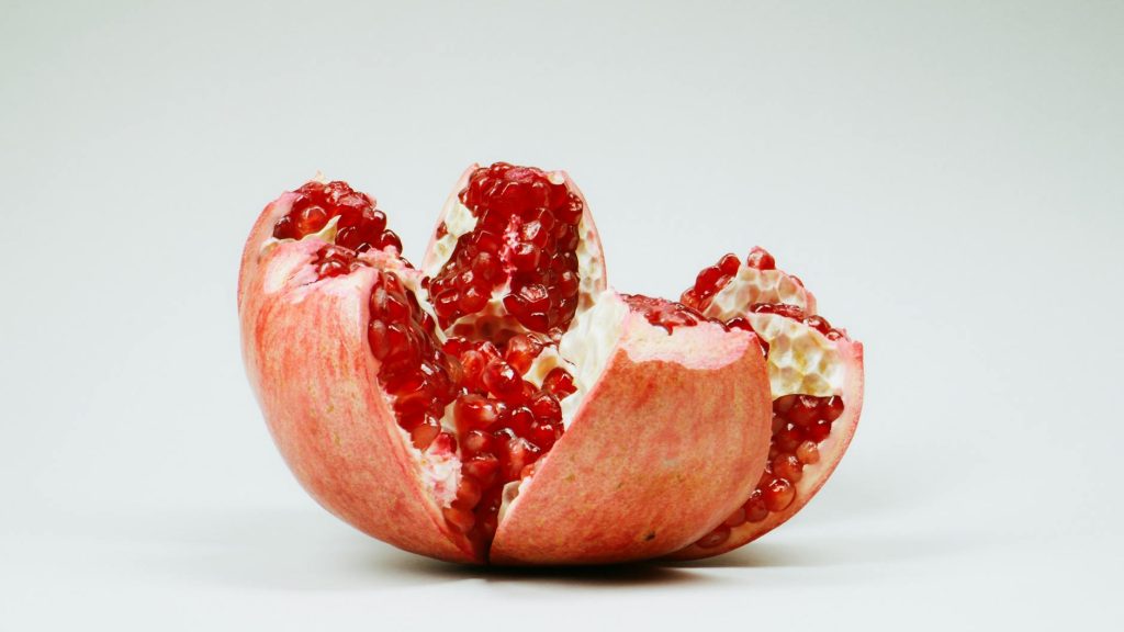 A detailed image of a sliced pomegranate with red seeds on a white background.