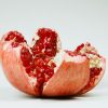 A detailed image of a sliced pomegranate with red seeds on a white background.