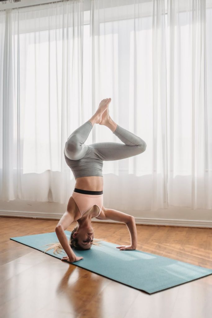 A woman in activewear performing a yoga headstand indoors, showcasing strength and balance.
