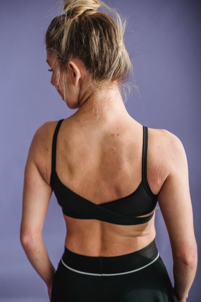 Young woman in activewear showing back muscles against a purple background.